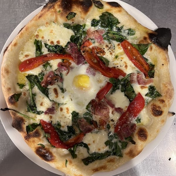 HillCrust Pizza's pizza with a fried egg, spinach, red peppers, and bacon on a white plate.