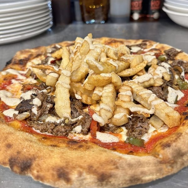 HillCrust Pizza's cheesesteak pizza, topped with steak, peppers, onions, and french fries drizzled with sauce.