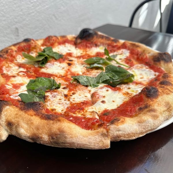 A freshly baked HillCrust Pizza Margherita, topped with vibrant basil leaves, sits on a dark table.
