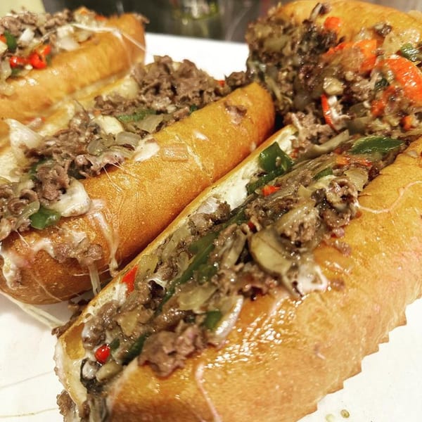 Close-up of multiple HillCrust Pizza cheesesteak sandwiches with melted cheese, steak, onions, and peppers.