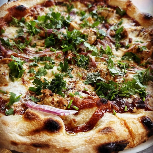 Close-up of a HillCrust Pizza with chicken, red onions, cilantro, and BBQ sauce.